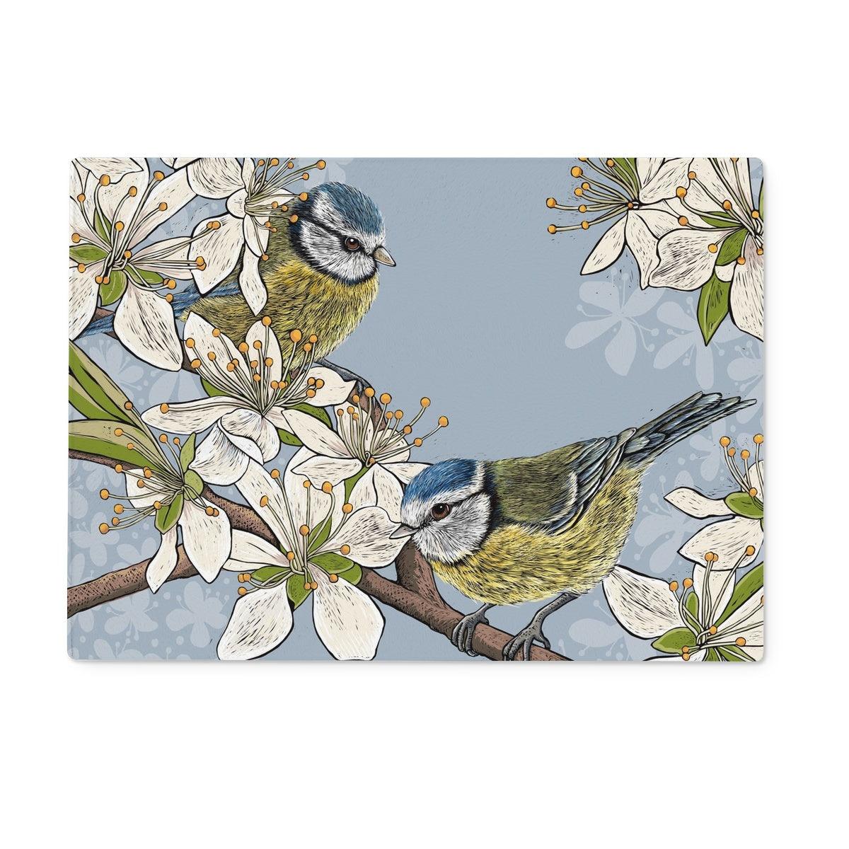 This design from Fox and Boo depicts two cute blue tits perched on stems of a hawthorn blossom tree, background is grey blue.