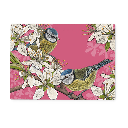 This design from Fox and Boo depicts two cute blue tits perched on stems of a hawthorn blossom tree, background is deep pink.