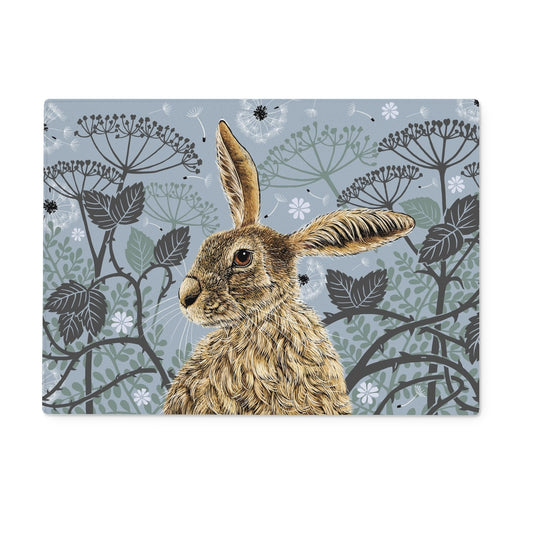 This coaster design features a hare portrait with one floppy ear, around the hare are stylised brambles, leaves, cow parsley and dandelion puffs, background colour is a blue  grey.