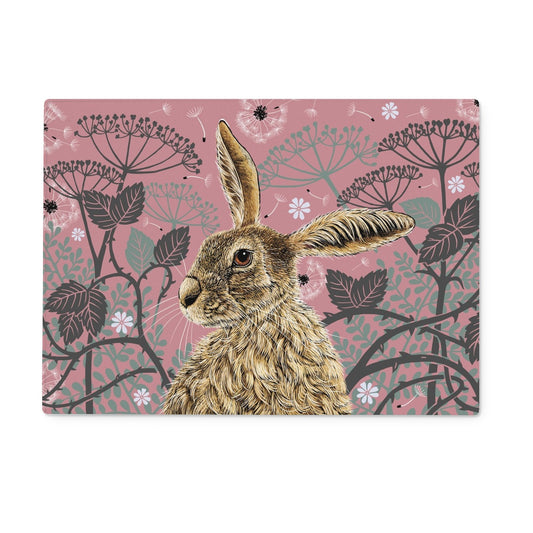 This worktop saver design features a hare portrait with one floppy ear, around the hare are stylised brambles, leaves, cow parsley and dandelion puffs, background colour is an antique rose pink.